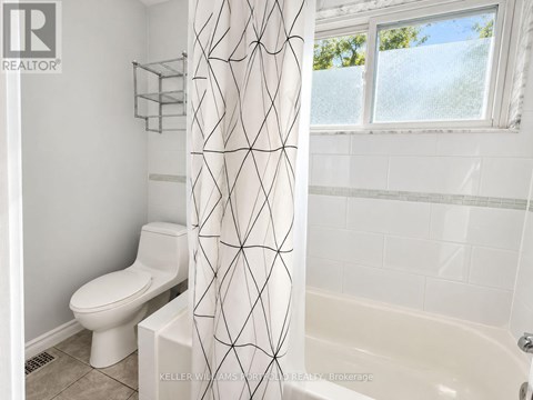 A white toilet sits next to a white shower curtain in a bathroom.