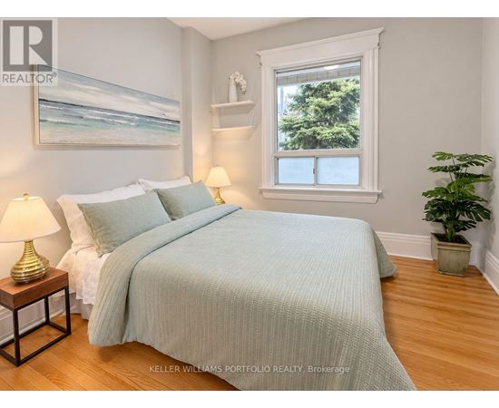 A bedroom with a bed, two lamps, a painting, and a potted plant.