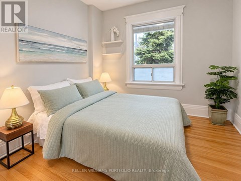 A bedroom with a bed, two lamps, a painting, and a potted plant.