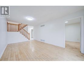 A spacious room with wooden flooring and a staircase.