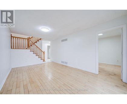 A spacious room with wooden flooring and a staircase.