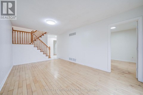 A spacious room with wooden flooring and a staircase.