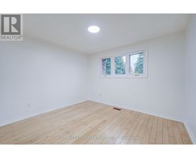 A room with wooden flooring and a window showing trees outside.