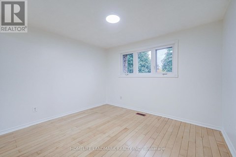 A room with wooden flooring and a window showing trees outside.