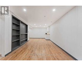 A spacious room with wooden flooring and white walls, featuring a row of shelves on the left side.