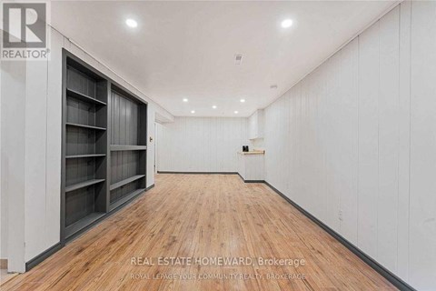 A spacious room with wooden flooring and white walls, featuring a row of shelves on the left side.