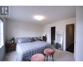 A bedroom with a bed, a pink stool, and a window.