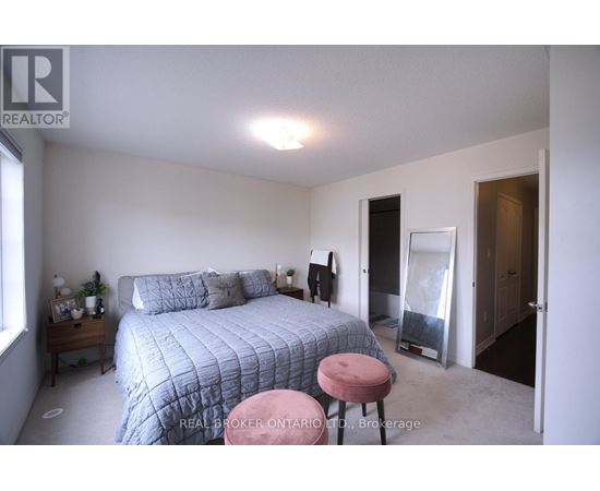 A bedroom with a bed, a pink stool, and a window.