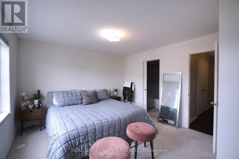 A bedroom with a bed, a pink stool, and a window.