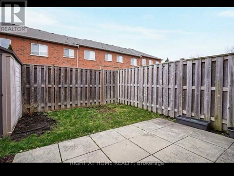 A backyard with a wooden fence and a brick building in the background.