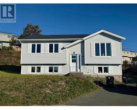 A house with a grey roof and white siding is surrounded by a grassy area and a clear blue sky.