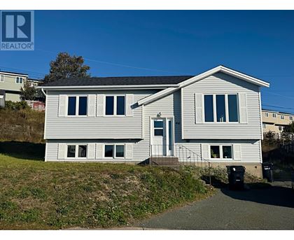 A house with a grey roof and white siding is surrounded by a grassy area and a clear blue sky.