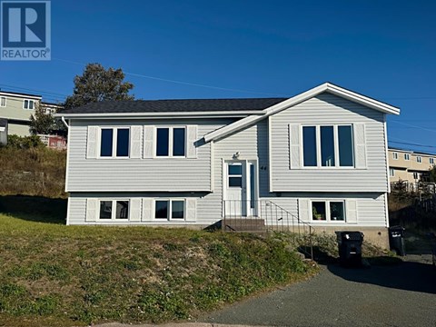 A house with a grey roof and white siding is surrounded by a grassy area and a clear blue sky.