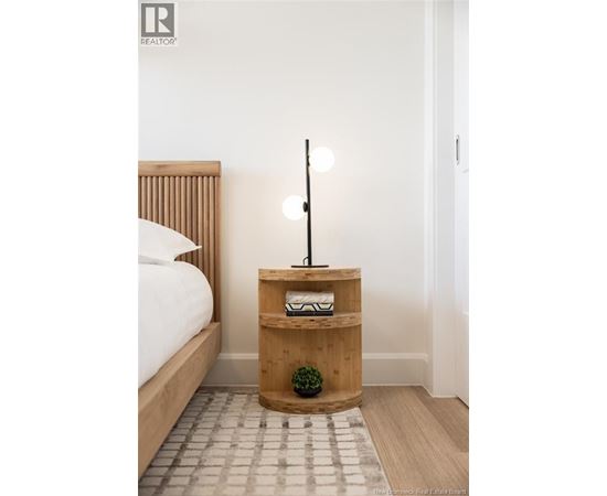 A bedroom with a bed, a wooden nightstand with a plant and a lamp.