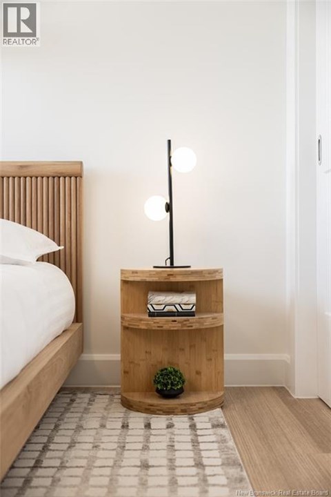 A bedroom with a bed, a wooden nightstand with a plant and a lamp.