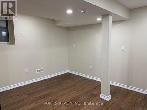 A room with wooden flooring and a white pillar in the middle.
