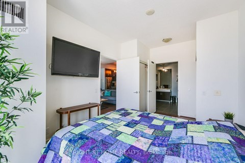 A bedroom with a bed covered in a patchwork quilt and a flat screen TV mounted on the wall.