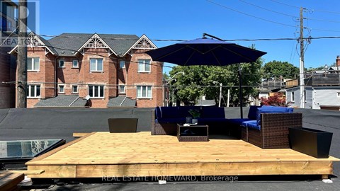 A wooden deck with a blue umbrella and chairs is in front of a brick building.