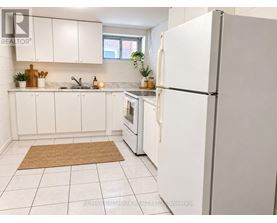 A white refrigerator stands in a kitchen with white cabinets and a brown rug on the floor.