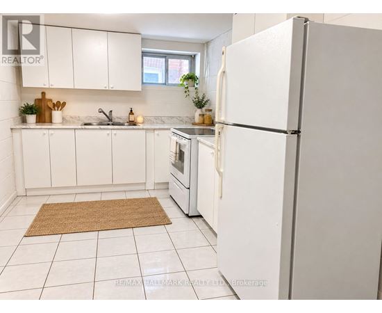 A white refrigerator stands in a kitchen with white cabinets and a brown rug on the floor.