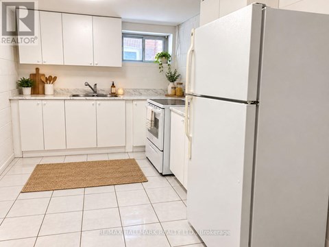 A white refrigerator stands in a kitchen with white cabinets and a brown rug on the floor.