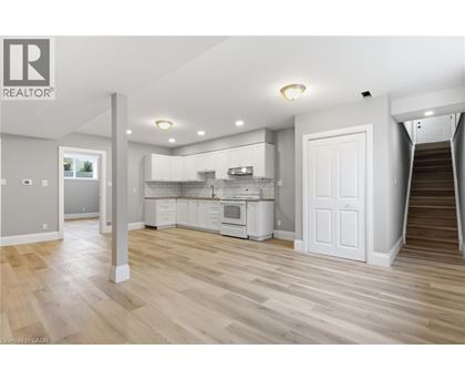 A spacious kitchen with white cabinets and a staircase leading to another room.