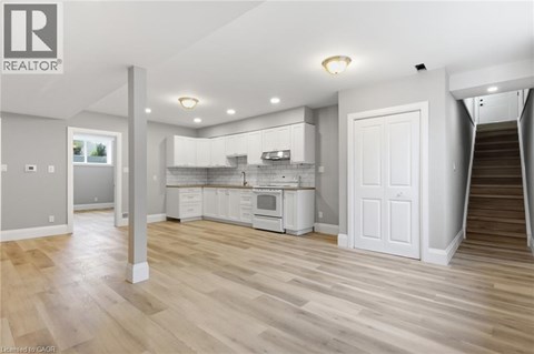 A spacious kitchen with white cabinets and a staircase leading to another room.