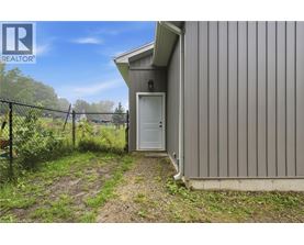 A small building with a white door is surrounded by a fence and vegetation.