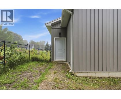 A small building with a white door is surrounded by a fence and vegetation.