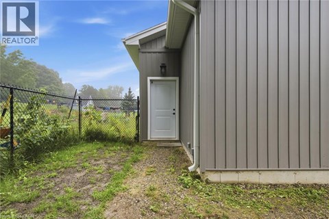 A small building with a white door is surrounded by a fence and vegetation.