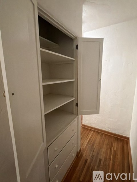 A white open wardrobe with shelves and drawers in a room with wooden flooring.