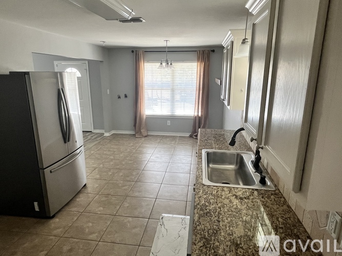 A kitchen with a black fridge, a sink, and a window with curtains.