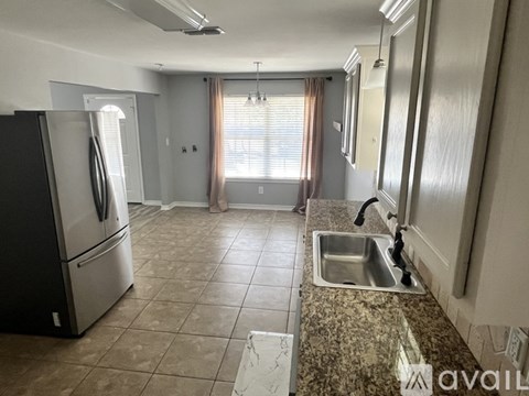 A kitchen with a black fridge, a sink, and a window with curtains.