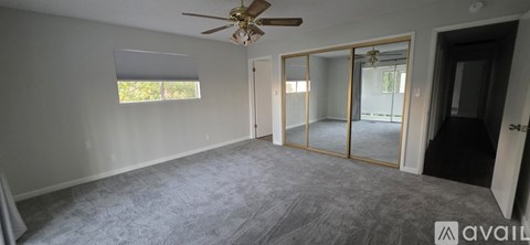 A spacious room with a ceiling fan and sliding glass doors leading to a balcony.