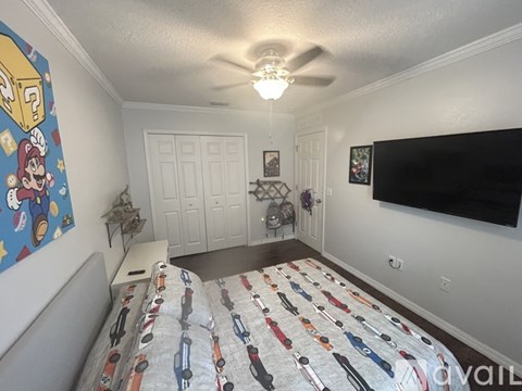 A bedroom with a bed covered in car-themed bedding and a Mario-themed painting on the wall.