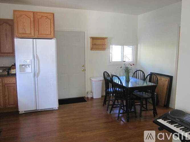A kitchen with a white fridge, wooden cabinets, a dining table with chairs, and a piano.
