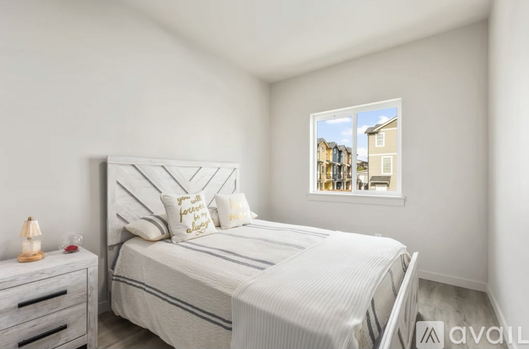 A bedroom with a bed, nightstand, and window showing a view of houses.