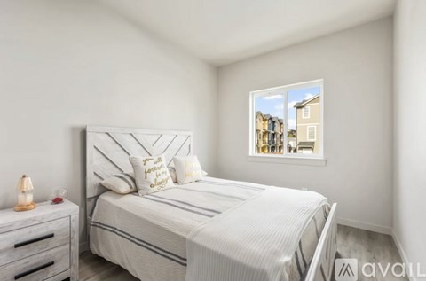 A bedroom with a bed, nightstand, and window showing a view of houses.