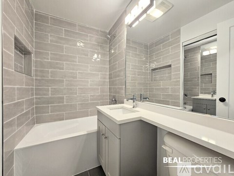 A bathroom with a white tub, sink, and grey tiled walls.