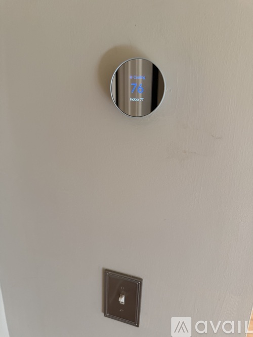 A round thermostat on a wall with the number 76 on it.