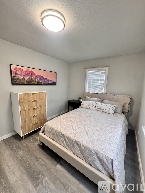 A bedroom with a bed, nightstand, and a painting on the wall.