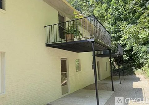A balcony with a black railing and a potted plant is attached to a yellow building.