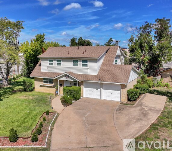 A house with a brown roof and a white garage door is surrounded by a green lawn and trees.