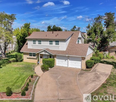 A house with a brown roof and a white garage door is surrounded by a green lawn and trees.