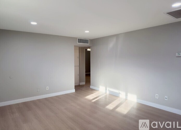 A spacious room with wooden flooring and a door on the right side.