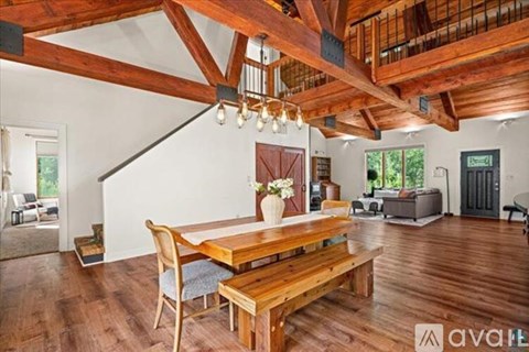 A wooden dining table with chairs is in the center of a spacious room with a high ceiling and wooden beams.