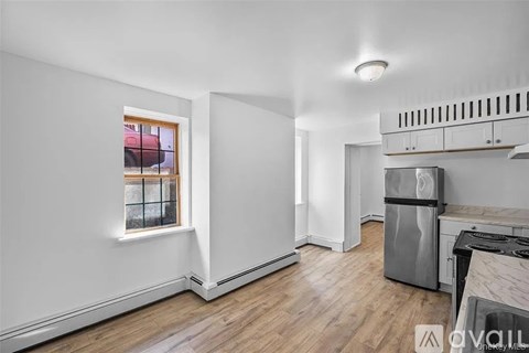 A kitchen with a stove top oven and a window with a view of a red car and a fence.