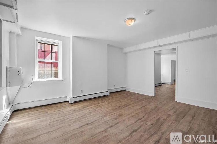A spacious room with wooden flooring and a window with red curtains.