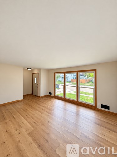 A room with wooden flooring and a view of the outside through the windows.
