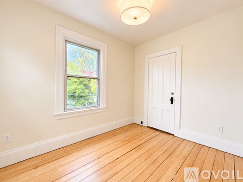 A room with a white door and a window with a view of trees.